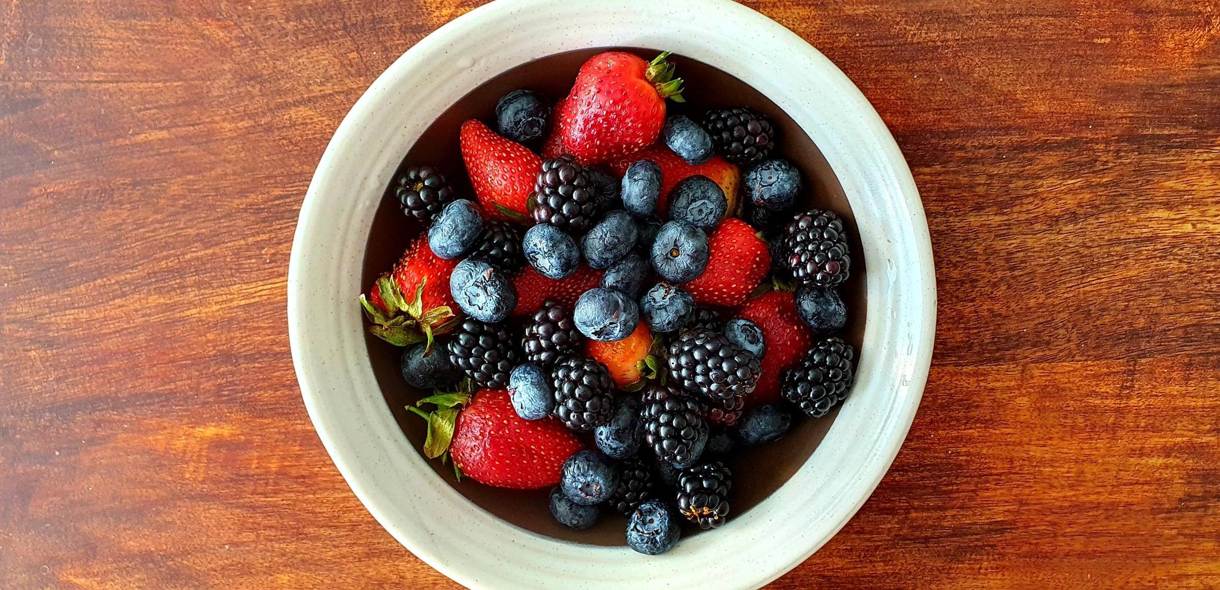 Schale mit Erdbeeren, Brombeeren und Heidelbeeren auf Holz