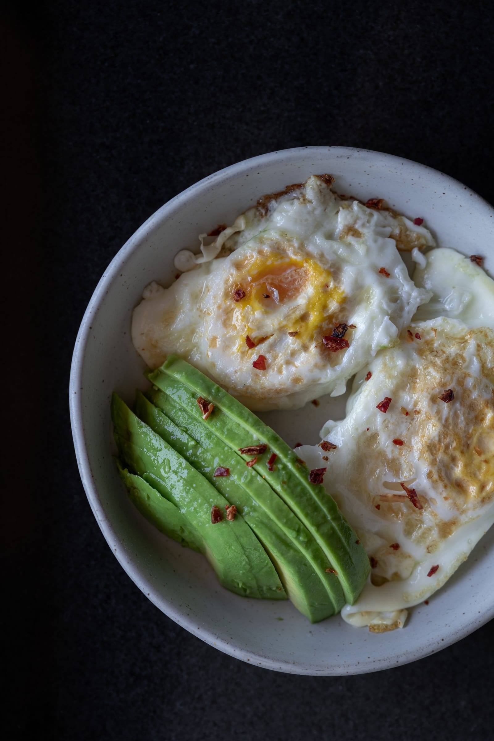 Zwei Spiegeleier mit Chiliflocken und Avocadoscheiben in einer Schale