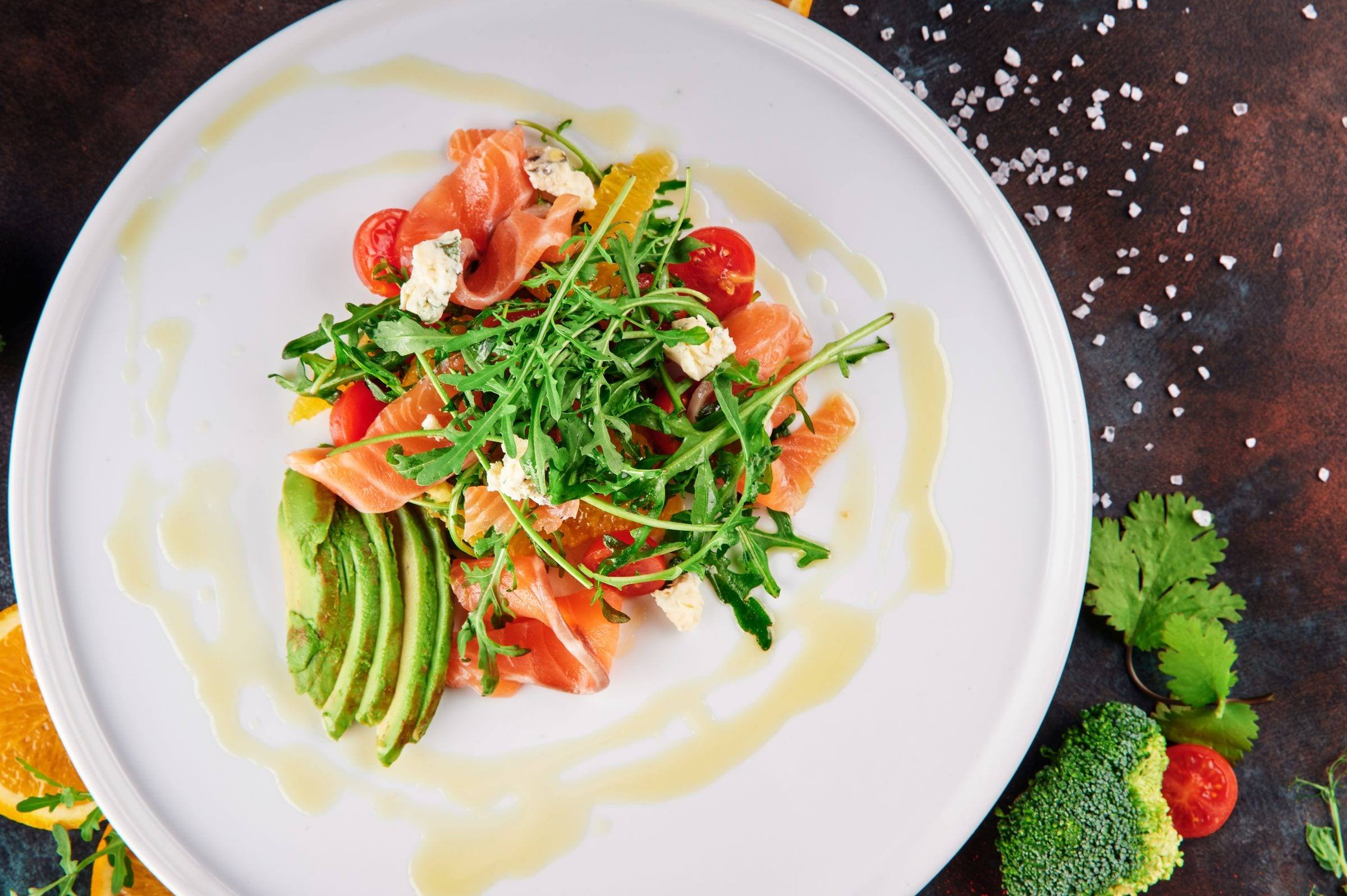 Teller mit Rucola, Räucherlachs, Avocadoscheiben, Kirschtomaten und Feta von oben