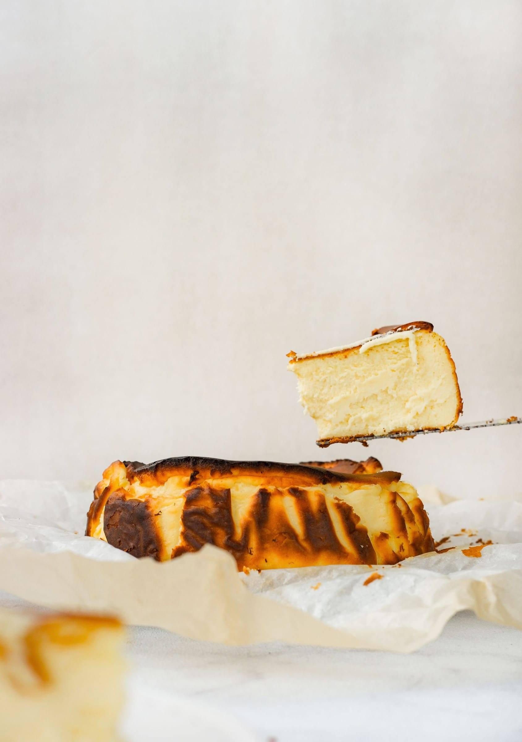 Käsekuchen nach baskischer Art mit dunkler Oberfläche, ein Stück wird herausgehoben