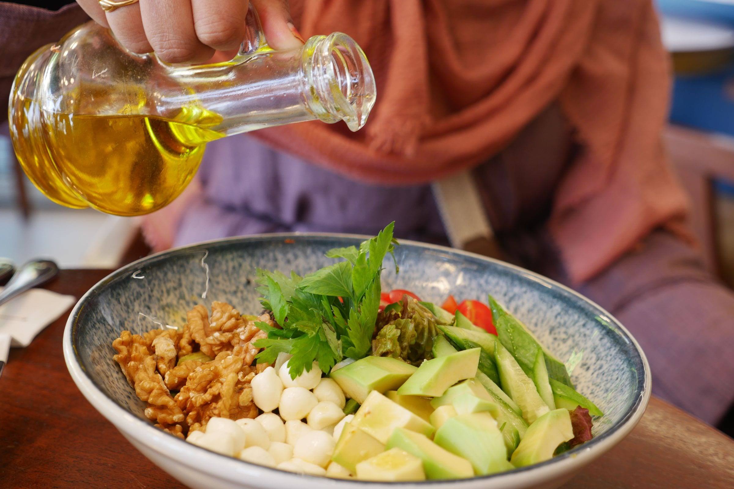 Olivenöl wird über eine Schale mit Salat, Walnüssen, Avocado und Wachteleiern gegossen