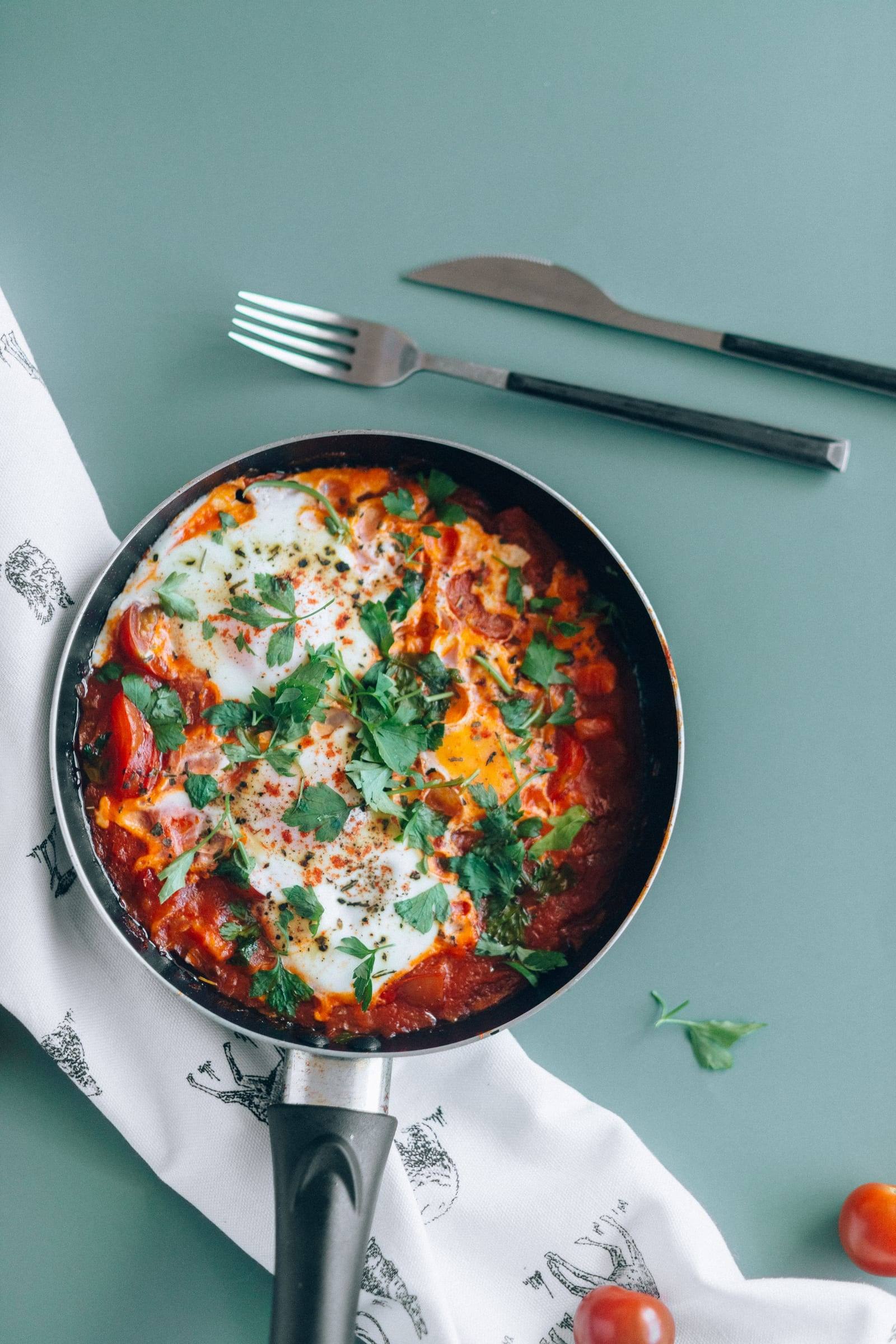 Shakshuka mit gestockten Eiern in Paprika-Tomaten-Sauce und Petersilie in einer Pfanne