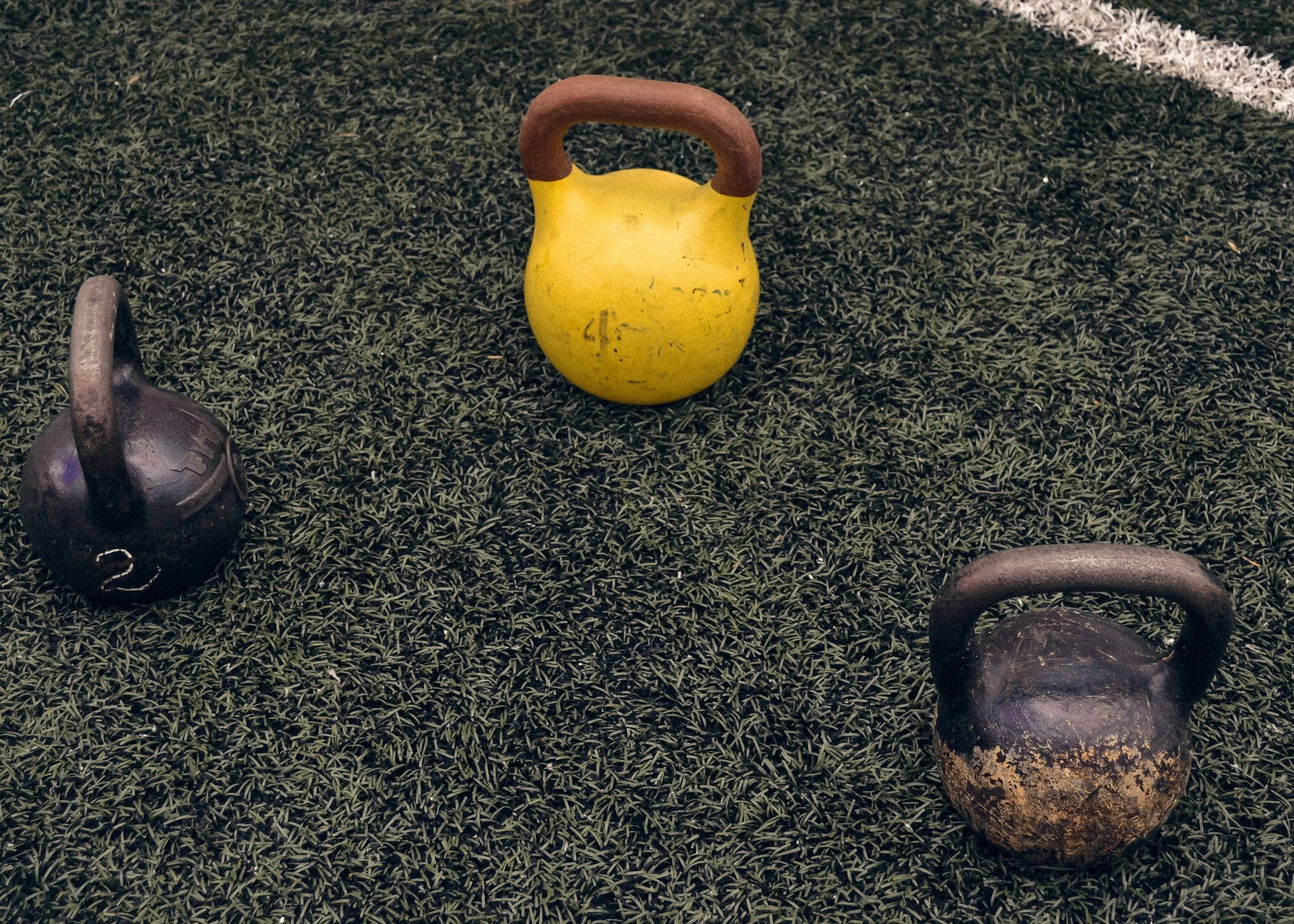 Drei Kettlebells auf Kunstrasen, eine davon gelb
